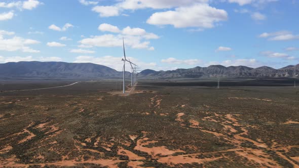 Drone aerial moving towards renewable energy wind farm in country desert Australia with mountains in