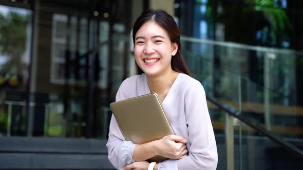 Successful and Happy Young Adult Business Woman Holding a Laptop with Smile Outside Corporate Office