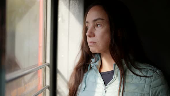 a Brunette with Long Hair Leans Against the Wall and Attentively Looks Out the Window in a Traveling