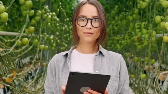 Young Woman Using or Playing Tablet in Greenhouse. Green Plant Growing in Warm House.