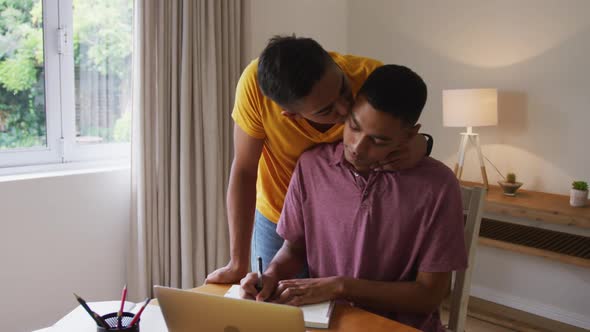 Mixed race gay male couple talking and embracing one sitting at desk working