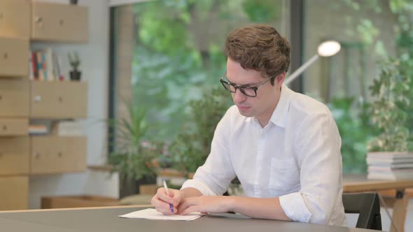 Young Man Writing on Paper in Modern Office