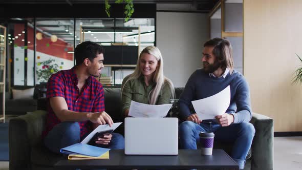 Diverse business people sitting using laptop and goign through paperwork in modern office