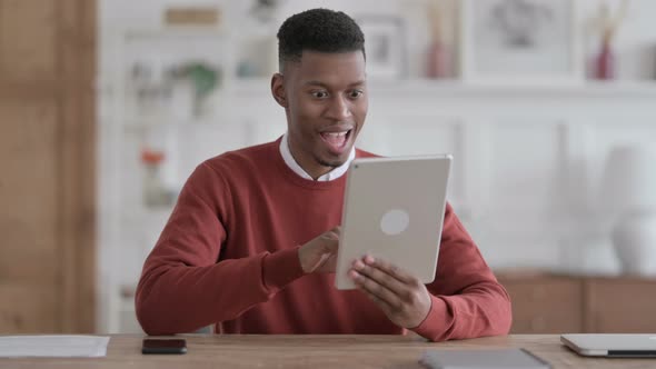 African Man Celebrating Success on Tablet in Office