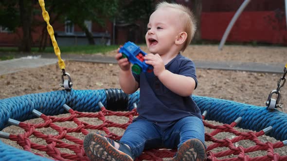 Happy Little Toddler Boy Swings on a Round Swing