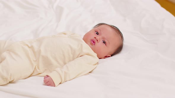 happy newborn baby lying on a white bed and blanket comfortable