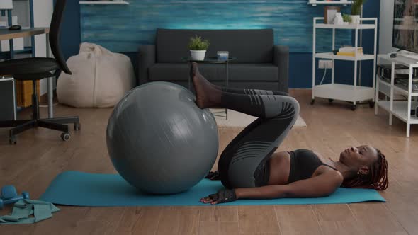 Athletic Woman with Black Skin Working Abs on Swiss Ball in Living Room