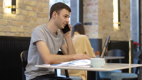 Young Millennial Successful Businessman Talking on the Phone and Typing on Laptop Keyboard