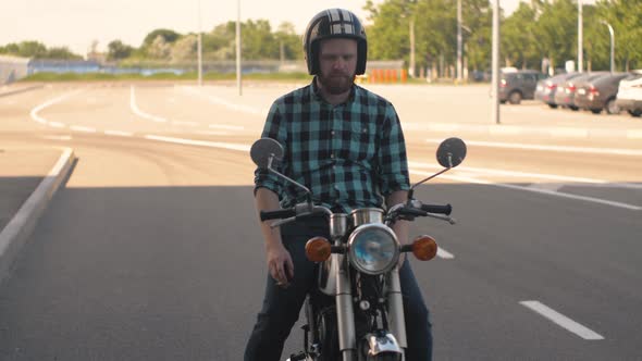 Portrait of Man Motorcyclist Smokes a Cigarette While Sitting on a Motorcycle at Street