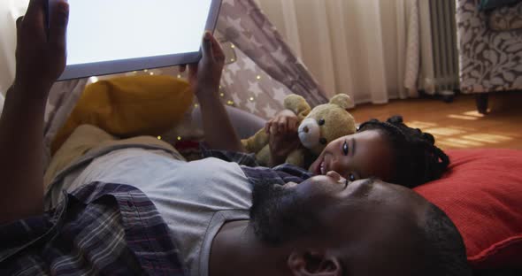 African american father and daughter lying in makeshift tent and using tablet with copy space