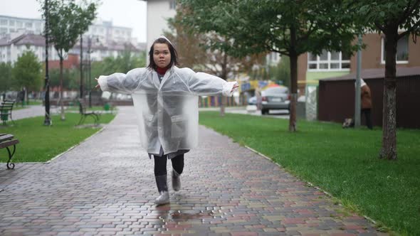 Young Cheerful Little Woman in Rain Coat Running Looking at Camera Leaving