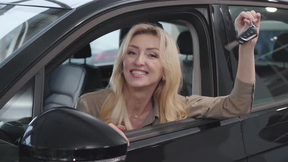 Happy Caucasian Woman with Blond Hair Sitting in Salon and Bragging Car Keys