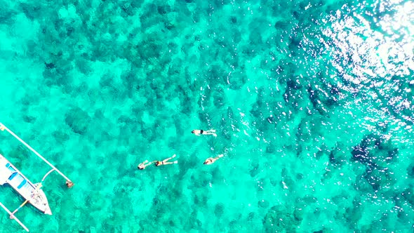People snorkel and swim close to an Indonesian boat, watching under clear turquoise water for tropic