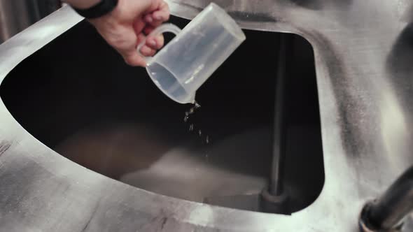 Brewery worker pours an important ingredient into a vat of malt