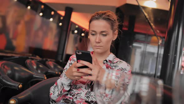Young Female French Uses Social Networks To Communicate with a Mobile Phone. Sits in a Restaurant