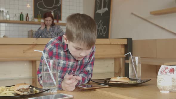 Little Boy Gaming on Phone While Eating in Cafe