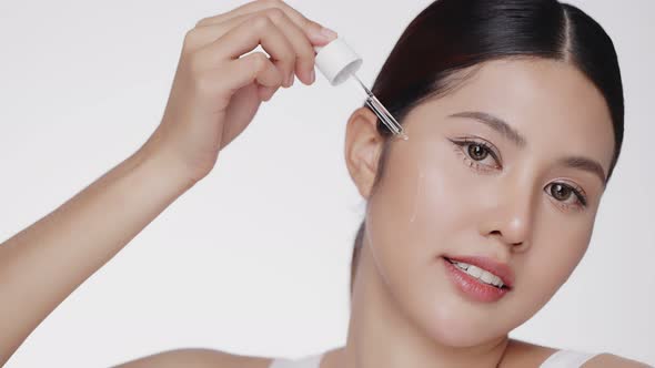 Young Asian beautiful woman dropping serum on face. Woman putting anti-ageing moisturizing serum.