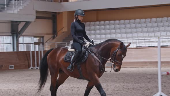 A Horsewoman Slowly Riding a Brown Horse on Arena