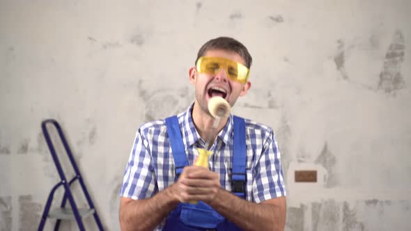 Cheerful Funny Male Builder Sings and Dances on Background of Repairs in House