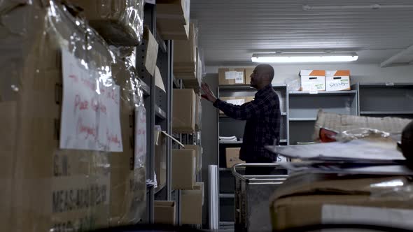 UK Indian Male Wearing Check Shirt Searching Through Different ShelvesIn Office Basement. Locked Off