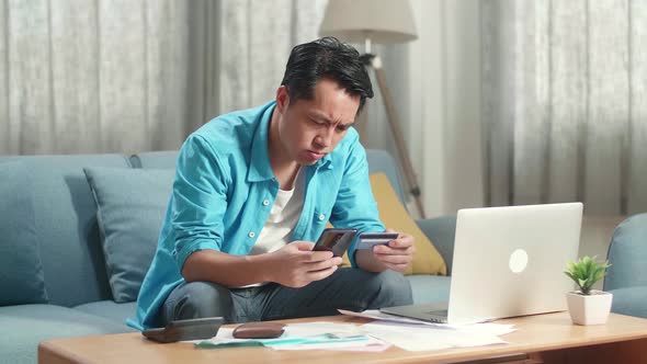 Asian Man With A Laptop Holding Credit Card And Smartphone Shaking His Head Due To Unable Pay Money