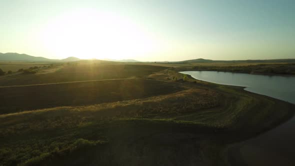 Flying Up Over Dam And Golden Fields At Sunset