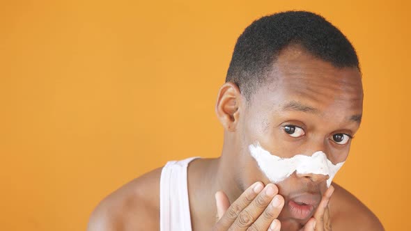 Young African American Man Applies a White Mask on the Face Smiling at the Camera, Isolated