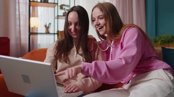 Young Adult Women Couple Looking at Laptop Notebook Screen Making Online Shopping Purchase at Home