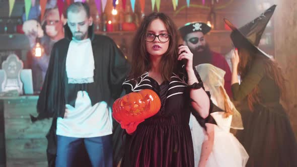 Young Attractive Girl in Witch Costume Dances with a Jack-o-lantern in Her Hands