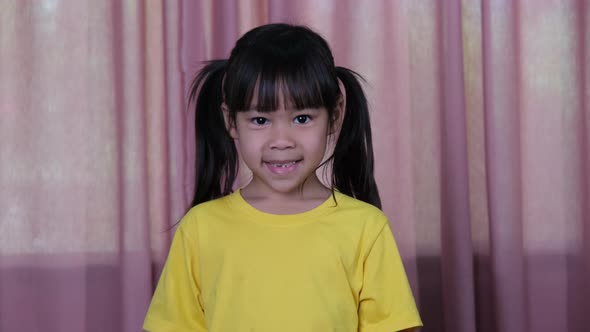 Portrait of a happy smiling little girl on a pink curtain background at home.