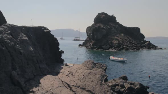 A rocky beach within the Santorini caldera with catamarans floating around it.