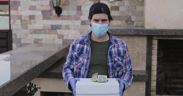 Man in Mask and Gloves Shows Order in Box with Some Money on It at Camera