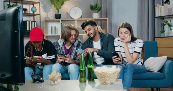 Friends Sitting on the Couch at Somebody's Home and Use Smartphones to Watch Apps or Videos