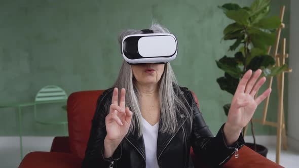 Woman with Gray Hair in Trendy Clothes which Sitting in the Cozy Chair in Virtual Reality Headset