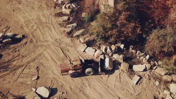 yellow bulldozer with a bucket is carrying a large stone near a sand quarry. Camera motion down.