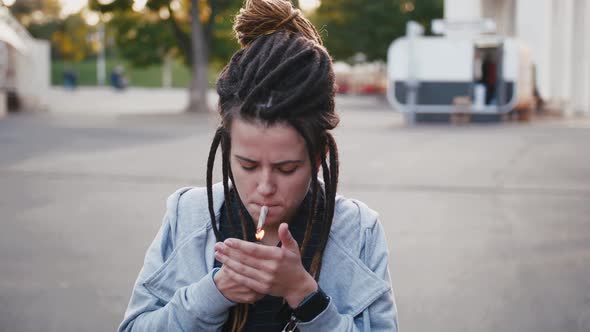 Portrait of Young Pretty Woman with Dreadlocks Smoking Marijuana Joint in Park Slow Motion