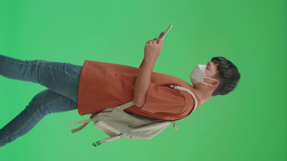 Side View Of Asian Boy Student Wearing A Mask, Using Tablet While Walking To School On Green Screen