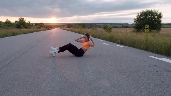 Athletic Girl Doing Abs Exercises Flexing Legs on Road at Summer Nature