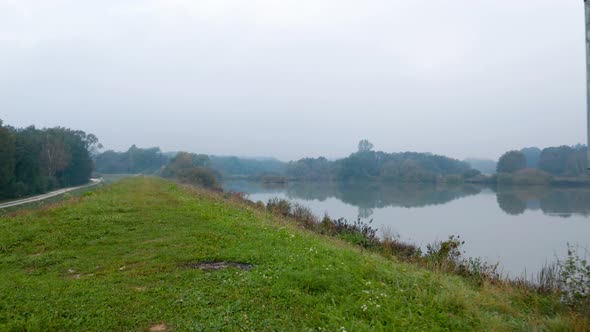 Pan out drone shot of a metal silo on a grassy hill overlooking a clear reflective lake on a misty a