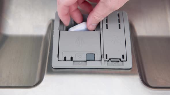 A Man's Hand Puts a Dishwasher Pill in a Closeup Dishwasher in the Kitchen