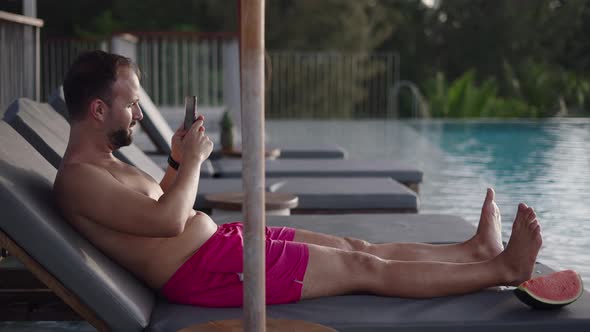 Side View of a Bearded Midage Man Resting on a Deckchair By the Pool and Taking Panoramic Photo with