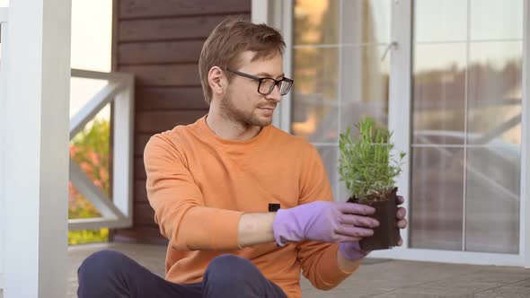 Young man gardener wearing gloves holding a young plant lavender in plastic pot.