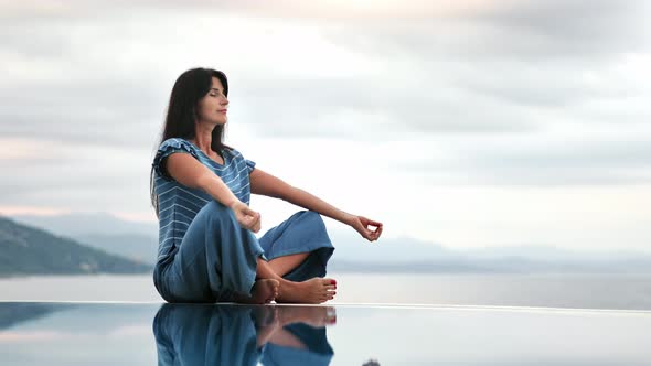 Relaxed Woman Enjoying Calmness Meditation Sitting in Lotus Position at Endless Swimming Pool Sea