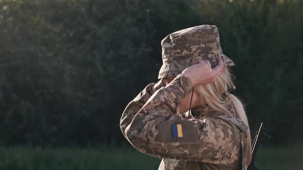 Female Soldier Puts on Camouflage Hat on Head Outdoors