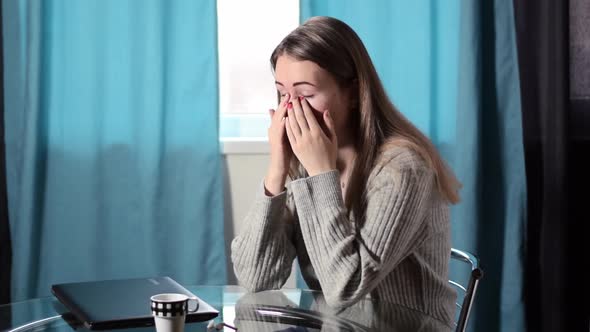 Tired young woman is rubbing her eyes after working online