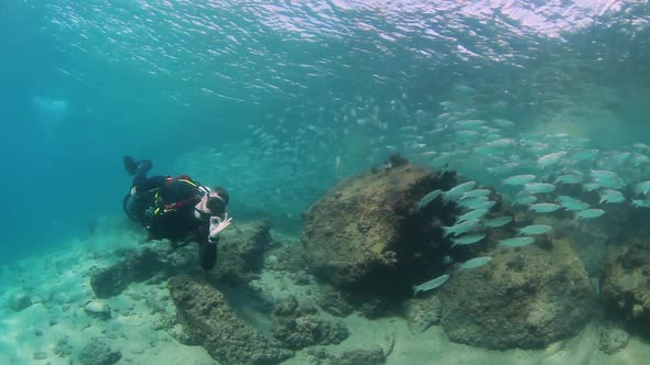 A scuba diver operating a underwater scooter near a large school of fish