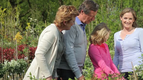 Grandparents, daughter and granddaughter looking at plants in garden centre