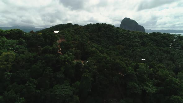 Aerial view flying over a tropical island with a dirt road, Philippine houses and green vegetation.