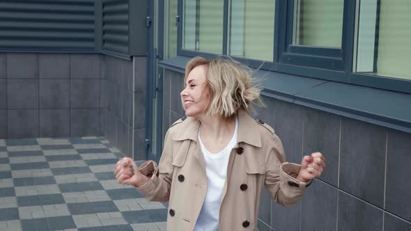 Cheerful Young Blonde Woman in Jacket Making Winner Gesture with Two Hands and Screaming Celebrating