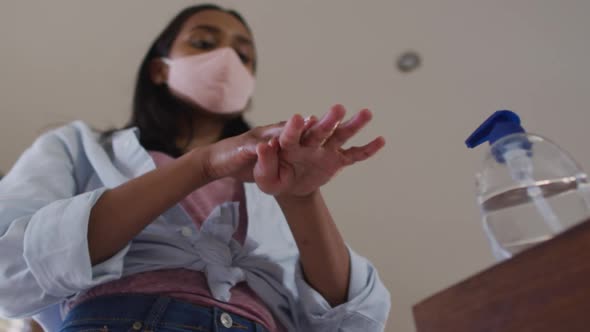 Mixed race woman wearing mask at home disinfecting hands